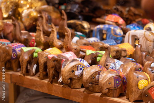 Collection of handcrafted wooden elephant figurines arranged on a display table and selling at a market or craft store.The elephants are carved from wood and decorated with colorful painted patterns.