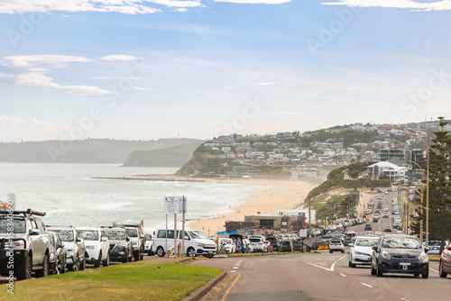 traffic on coastal road passing free public carpark for Australian beach on hazy afternoon