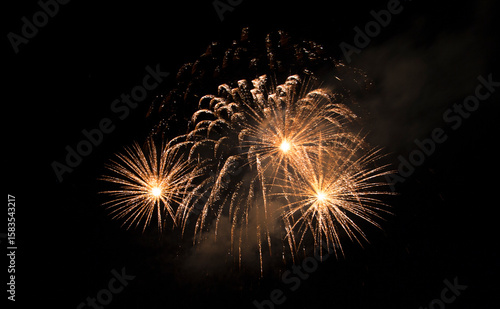 Quadro em tela Several golden fireworks explode simultaneously, illuminating the dark night sky with bright, streaking lights and a touch of smoke