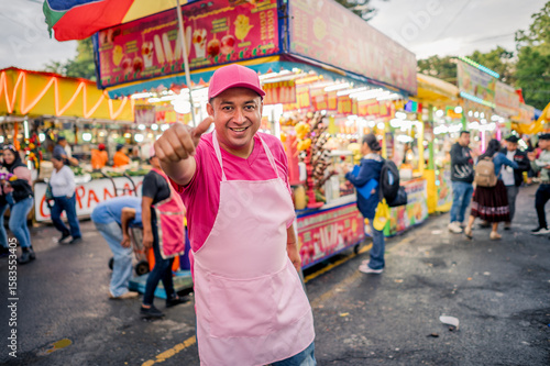 Portrait of a charismatic vendor selling his wares at a local fair in Latin America. The man is wearing pink clothing, with a food stand behind him.
