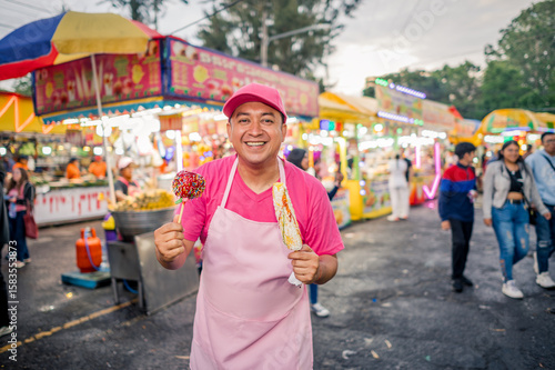 Portrait of a charismatic vendor selling his wares at a local fair in Latin America. The man is wearing pink clothing, with a food stand behind him.