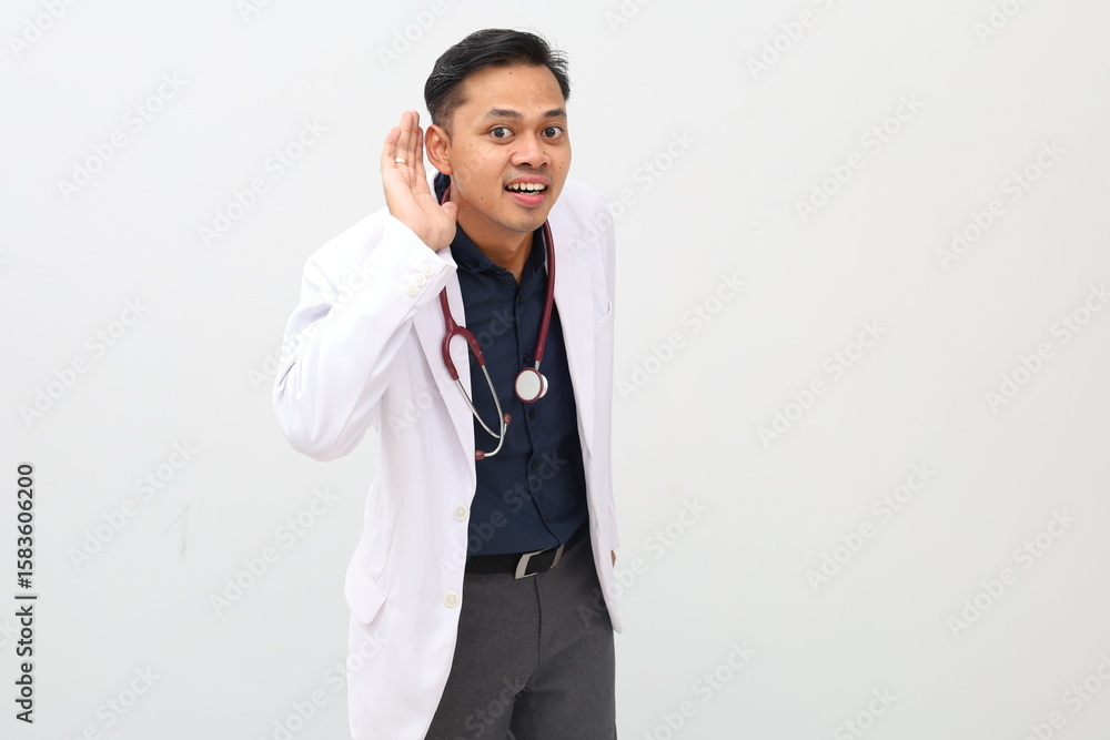 Male doctor wearing doctor's coat and stethoscope standing, hand next to ear gesture listening to something Male doctor wearing doctor's coat and stethoscope standing, hand next to ear gesture listening to something