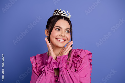 Canvas Print Elegant young woman wearing a tiara and vibrant pink dress posing on a purple ba