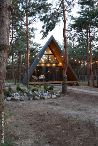 Modern A-frame cabin in a pine forest with hammock, trampoline, and string lights. Peaceful woodland retreat with cozy outdoor vibes
