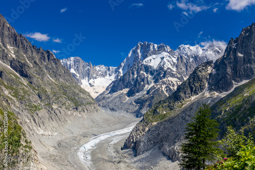 Beautiful mountain landscapes of the Alps on Tour du Montblanc hike. Green valley, snow summits and rocky peaks of Aiguilles de Chamonix and Montblanc. Summer sunny weather blue sky, trekking Alp hike