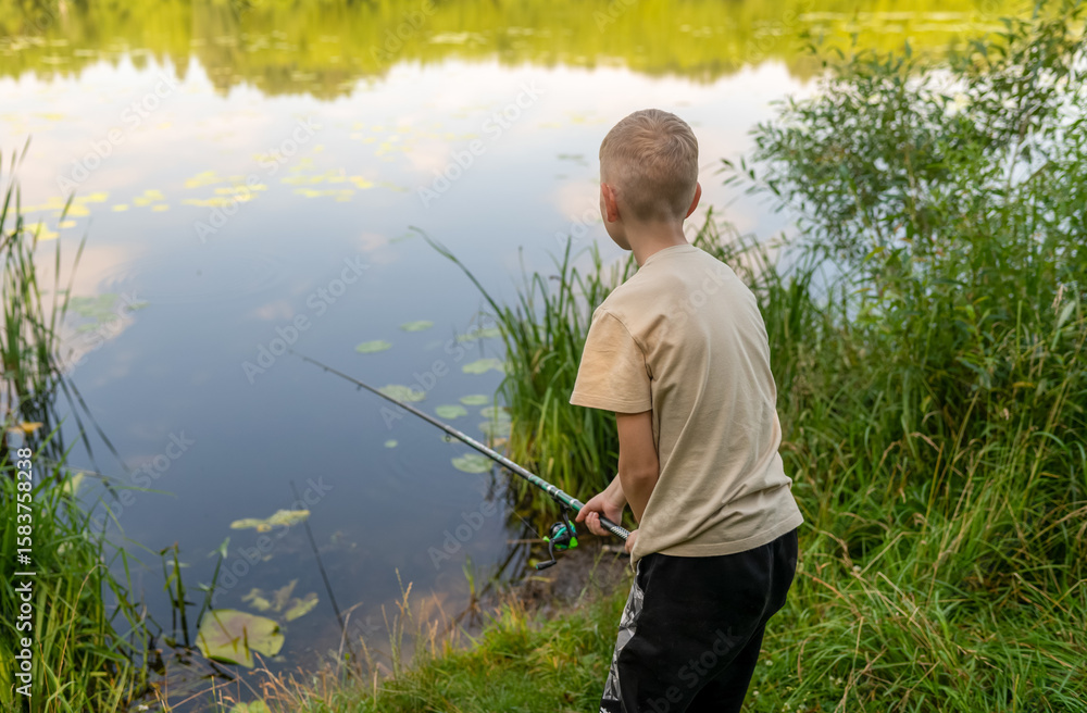 Boy waiting with fishing rod by calm river in green countryside Boy waiting with fishing rod by calm river in green countryside