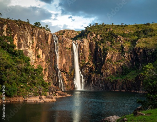 Majestic Waterfall Amidst Rugged Terrain: Witness the raw power and breathtaking beauty of nature's artistry as a magnificent waterfall cascades down sheer cliffs, nourishing a serene lake below.