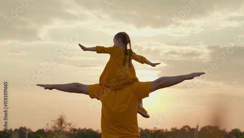 Tableau sur toile little child sits astride his father at sunset, the sun's dream of flying, the kid fantasizes about himself as pilot, girl daughter sits on her dad with her hands raised, happy family trip on weekend