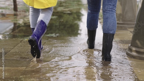 Photography people walk through puddles in rubber boots, heavy rainfall on asphalt, splashing puddles flying in different directions, lot of water flooding the road, the city's climatic changes, the environment