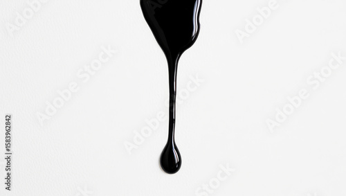 Close-up of a single glossy black drop of paint dripping on a white textured paper background under studio light
