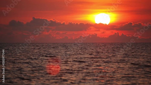 Large bright sun on red sky going down under the sea level at horizon on sunset, fast motion