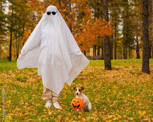 Fotografie Woman in white sheet and jack russell terrier dog holding jack o latrine in autumn forest