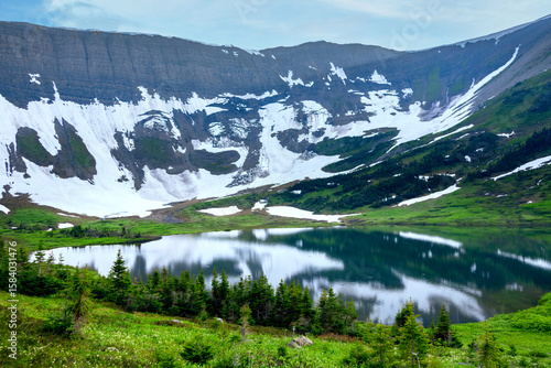 Scenic landscape of the beautiful lake among mountains covered with snow in spring and green foliage of willow and grasses. Tumbler Ridge geopark (Windfall lake), BC, Canada