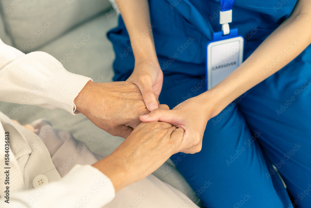 Fototapeta premium Asian woman caregiver holding senior woman hands and consoling with empathy. Doctor or nurse visit and take care elderly patient at nursing home. Home medical healthcare service and health insurance.