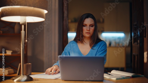 Late accountant reviewing papers making notes in copybook in evening home.