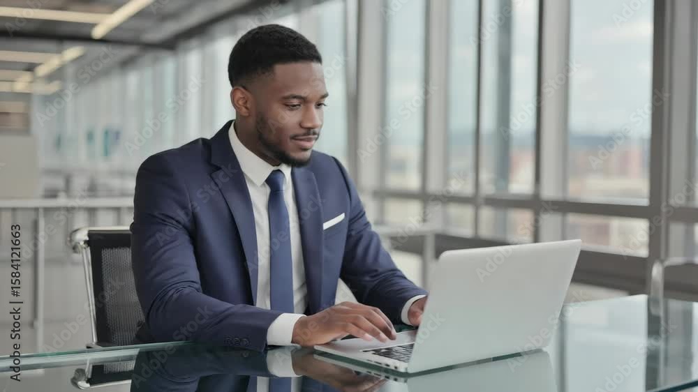 Man in suit sitting at desk with city skyline view, using laptop Man in suit sitting at desk with city skyline view, using laptop