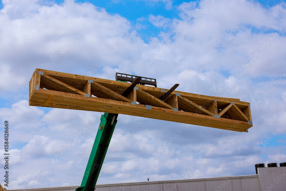 Fototapeta premium Crane hoists large wooden truss skyward against backdrop of works day indicating construction activity.