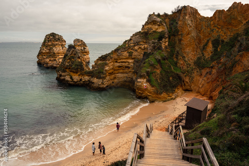 A beautiful high-angle view of Praia do Camilo in Lagos, showing tourists enjoying the sandy cove and turquoise waters at the bottom of the famous wooden staircase.