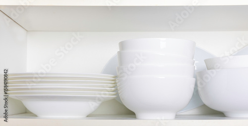Tableau sur toile White dishes and bowls in a kitchen cabinet.