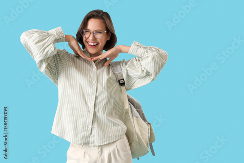 Happy female student with backpack showing tongue on blue background