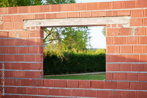 Unfinished brick wall with open window frame offering a peaceful view of the green garden in a future energy-efficient home.