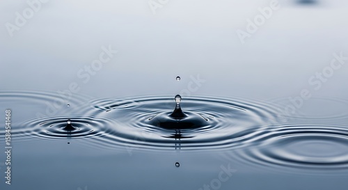 Fototapeta Naklejka Na Ścianę i Meble -  Close-up of a water droplet impacting a calm surface, creating ripples and a splash with reflections.