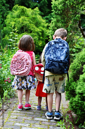 Three little siblings go hand in hand. Boy and two girls with school bags