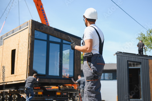 Bild auf Leinwand Construction worker supervising loading of modular house onto truck