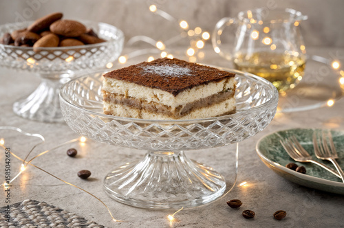  features a glass cake stand holding a layered cake, surrounded by coffee beans, a bowl of almonds, a pitcher, and a plate with forks, all set against a festive background with string lights.