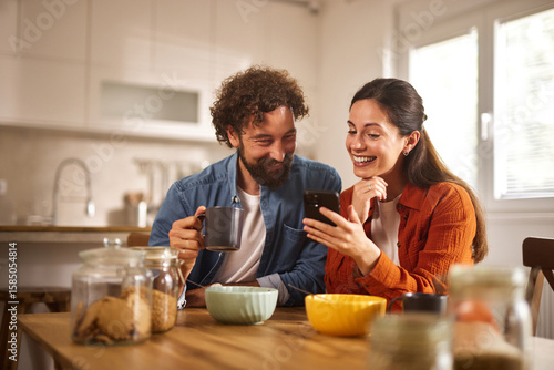 Konstfotografi Two individuals smile and engage with each other while sitting at a wooden table in a bright home office