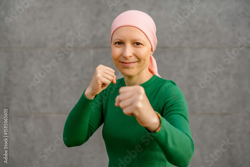 Self-confident woman with pink headscarf gesturing with her fists in her fight against cancer