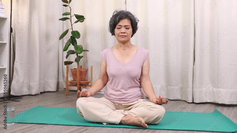 Asian elderly woman sitting cross-legged on yoga mat with hands on knees, practicing mindful breathing. The peaceful routine highlights senior, woman, yoga, breathing, wellness, meditation, lifestyle. Asian elderly woman sitting cross-legged on yoga mat with hands on knees, practicing mindful breathing. The peaceful routine highlights senior, woman, yoga, breathing, wellness, meditation, lifestyle.