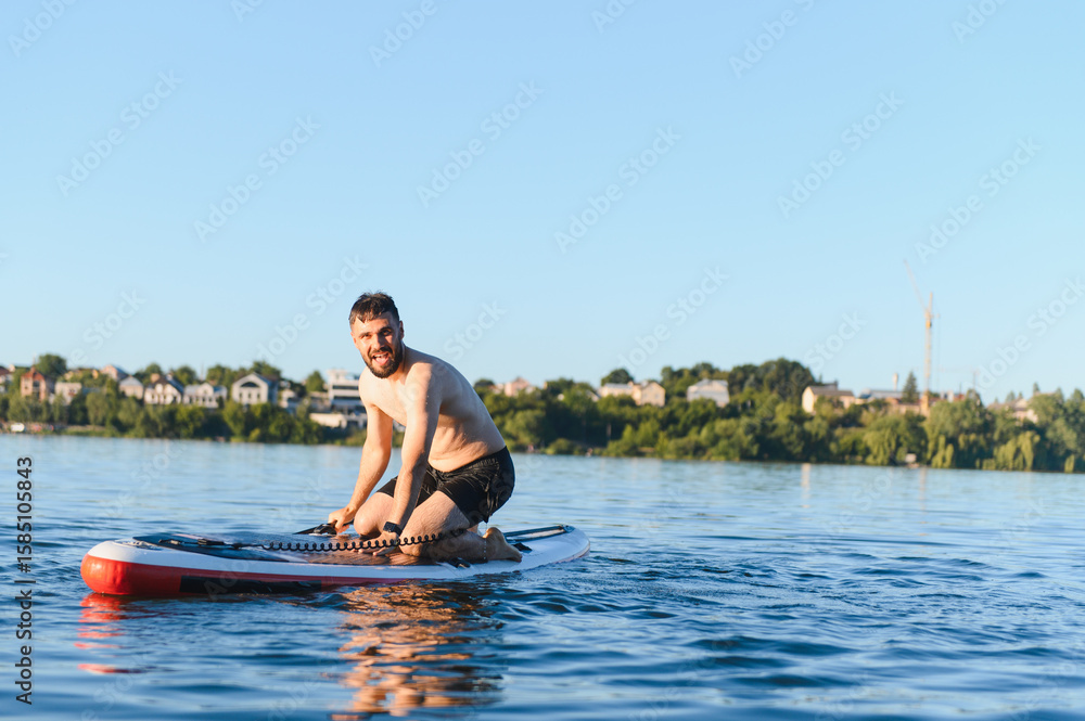 Fototapeta premium Man kneeling on paddle board enjoying paddle boarding on lake