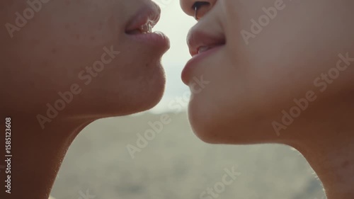 Passionate lesbian couple sharing tender moment while embracing and kissing on sandy beach during romantic sunset, expressing deep love and connection