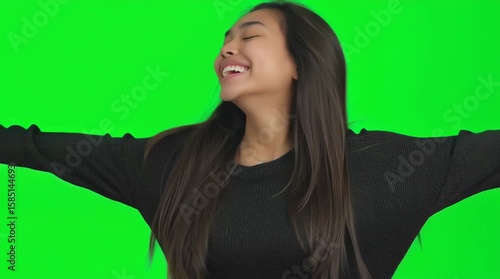A happy smiling young asian woman with crossed arms on a green screen. Female portrait for chroma key footage.
