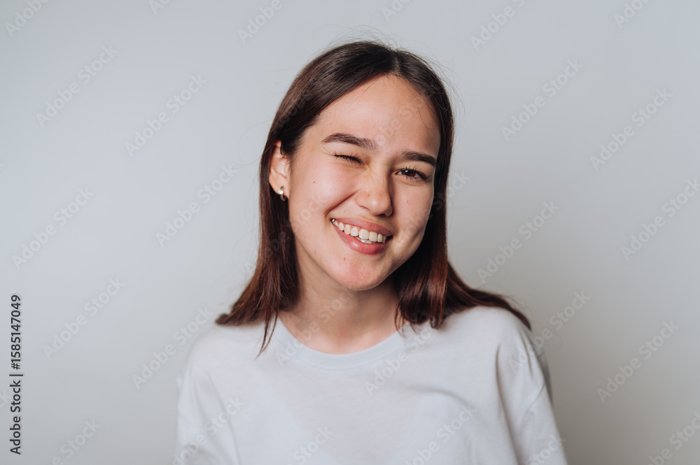 Smiling young woman winks at the camera while posing against a light background indoors Smiling young woman winks at the camera while posing against a light background indoors