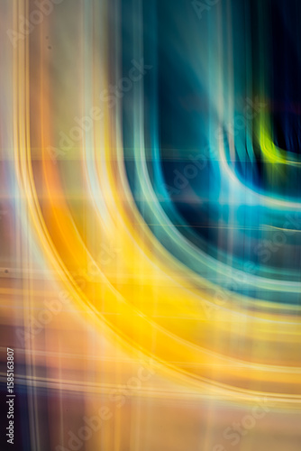 A digital abstract art piece featuring vibrant, overlapping yellow and orange light trails forming fluid, curving lines against a dark, blurred background.