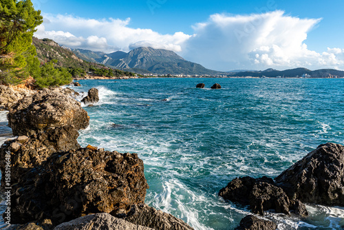 Stunning Adriatic coastline with turquoise waves crashing on rugged rocks, mountains in background. Great for travel, coastal nature, summer escape, adventure, and scenic destinations.
