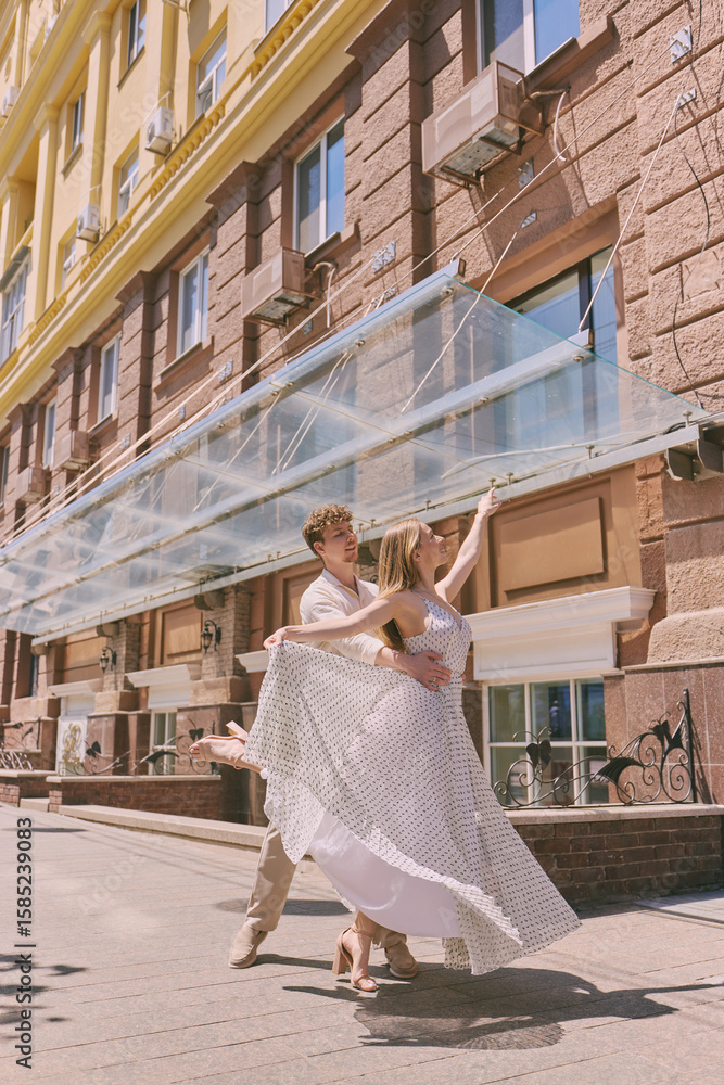 Obraz premium Elegant couple dances gracefully on a sunlit urban street with tall buildings adding to the urban charm. Concept of refined urban sophistication, dance and youth culture