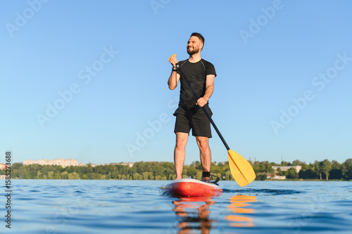 Foto Sportsman paddling on sup board on lake enjoying paddle boarding