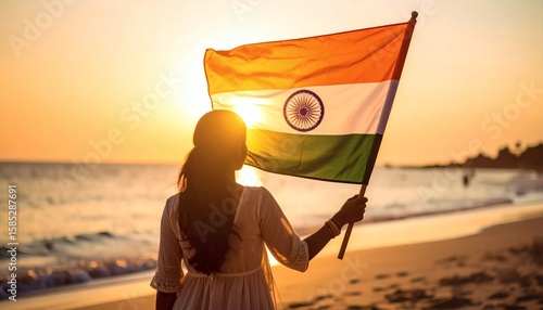 Silhouette of a person holding the Indian flag against a setting sun on a beach