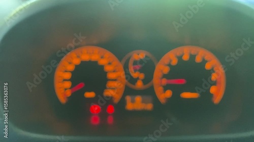 Blurred view of a car dashboard, with glowing orange gauges and indicators.