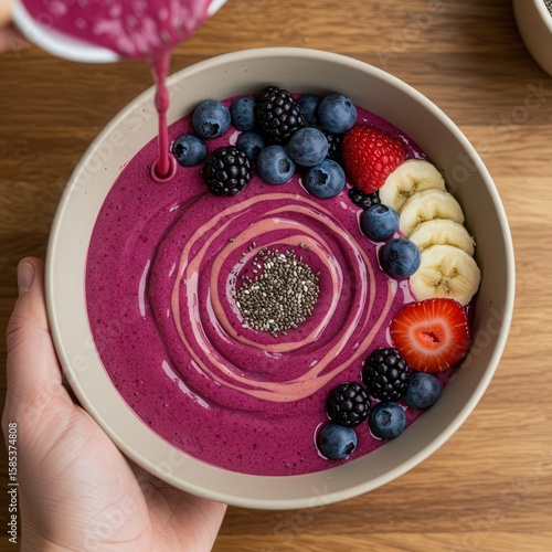 Vibrant smoothie bowl with berry fruits offers a refreshing and healthful culinary delight on a wooden surface.