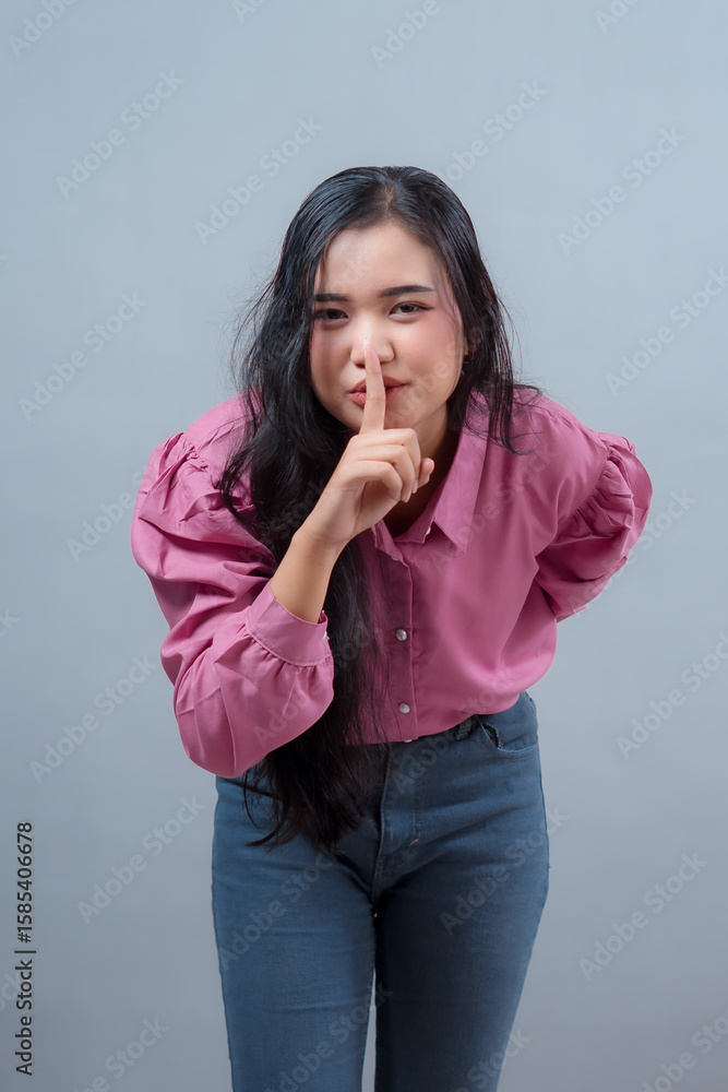 Charming Indonesian woman with long black hair making a quiet “shh” gesture, finger on lips, leaning slightly forward, smiling in playful expression. Studio shot, casual fashion look. Charming Indonesian woman with long black hair making a quiet “shh” gesture, finger on lips, leaning slightly forward, smiling in playful expression. Studio shot, casual fashion look.