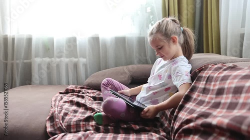 child girl uses a tablet sitting on the couch at home. Generation Z. gadget addiction. 