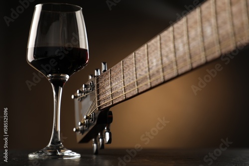 Photography Acoustic guitar and glass of red wine on black table, closeup