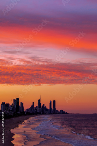 Red and orange colours in the sky over Gold Coast Australia, with surfer on the beach.