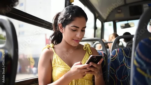 A young latina woman in a yellow dress smiles while using her smartphone on a city bus