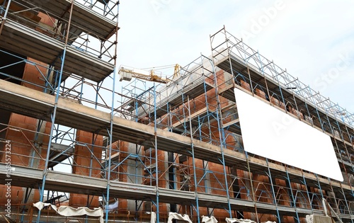 Wallpaper Mural Blank information board on the facade of a new large building under construction among the scaffolding. Tower crane and cloudy sky above. Background for copy space. Torontodigital.ca