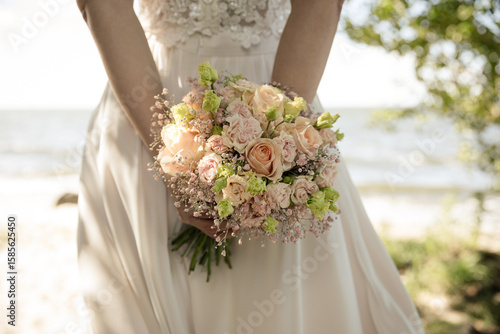 Fototapeta Naklejka Na Ścianę i Meble -  Braut hält romantischen Blumenstrauß am Strand – Sommerhochzeit in Pastellfarben